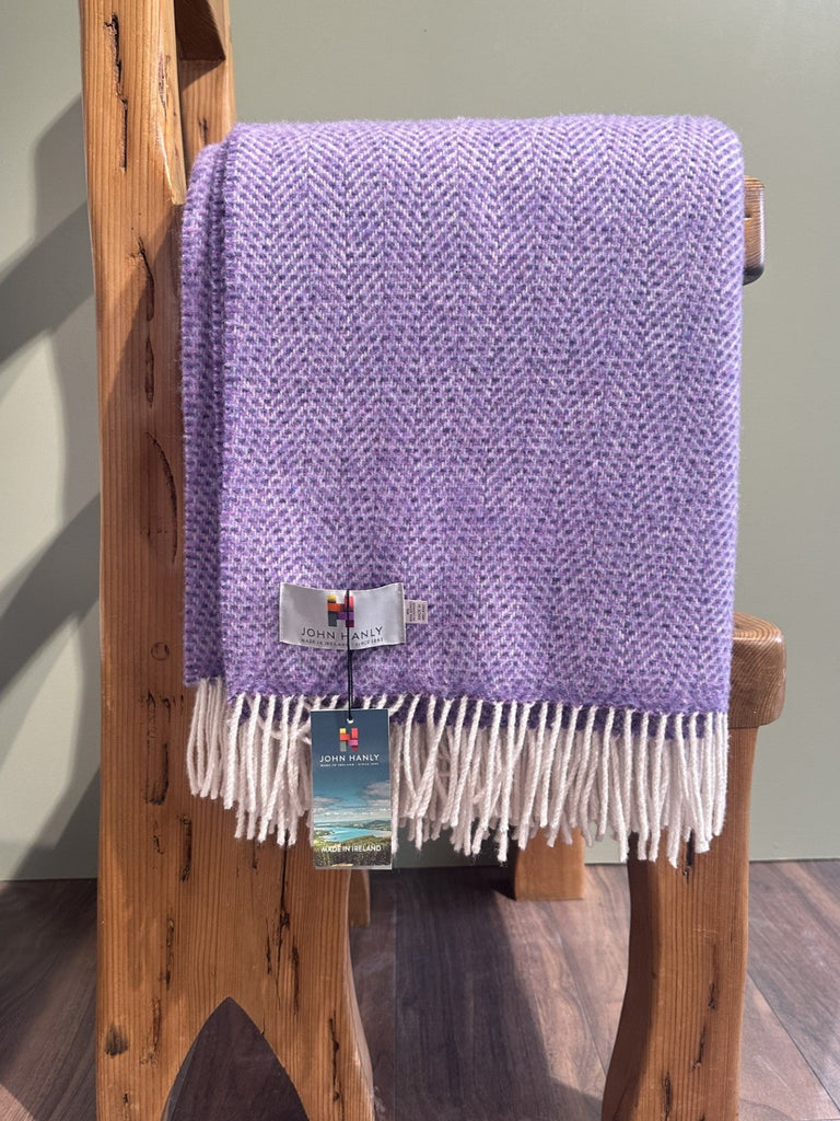 Purple blanket with white fringe draped over a wooden ladder against a light green wall.
